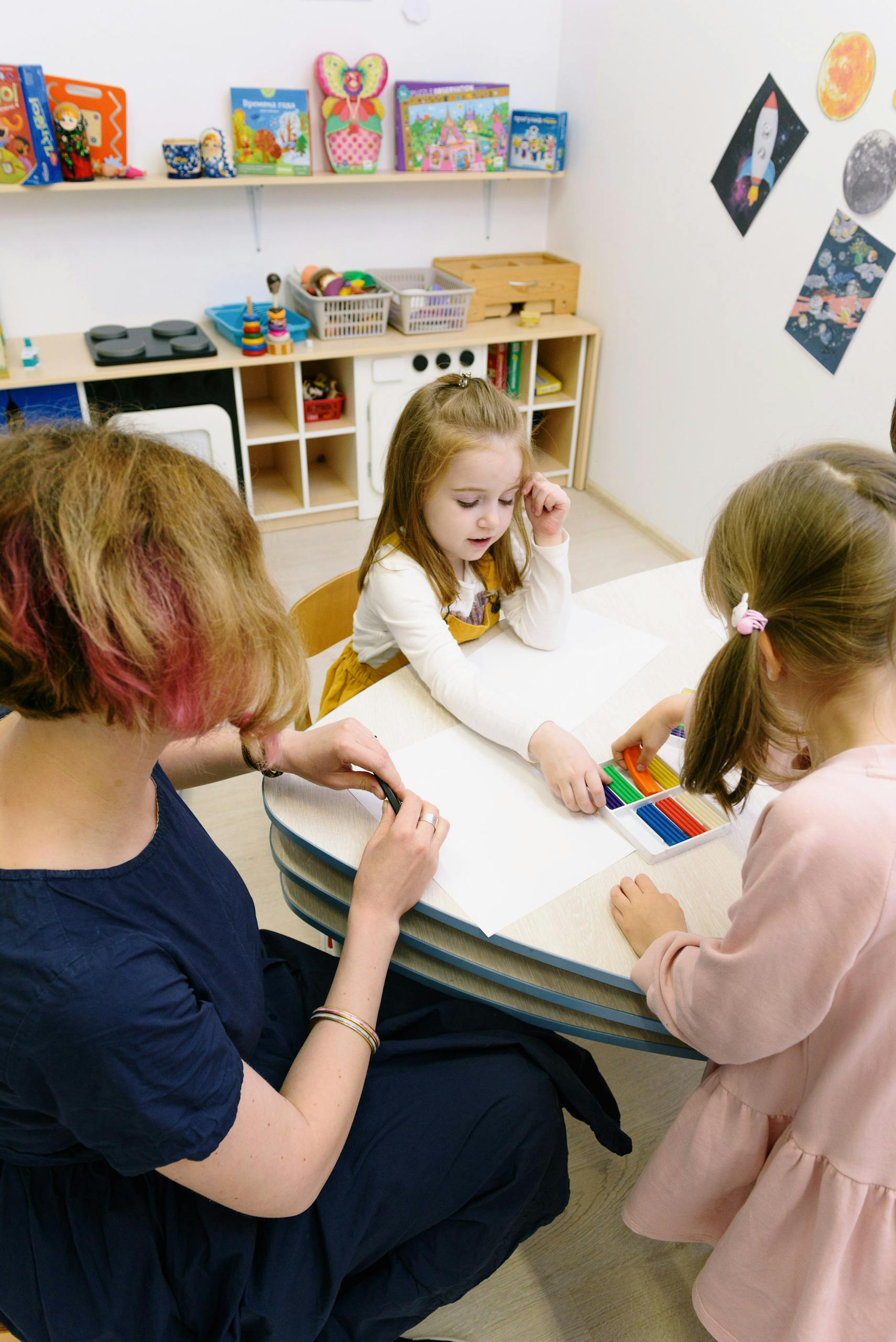 Children in a kindergarten engage in art activities guided by a teacher.